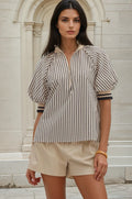 Woman wearing a striped shirt and beige shorts standing in front of a stone building.
