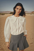 Woman wearing a white blouse with embroidery and gray shorts in a desert setting