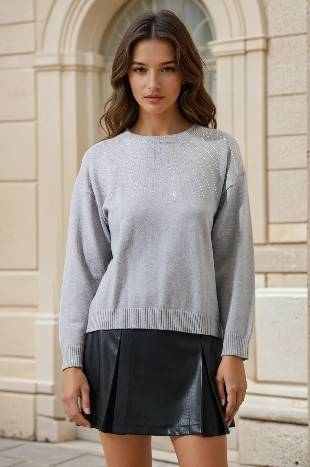 Woman wearing a gray sweater and black skirt standing in front of a stone building.
