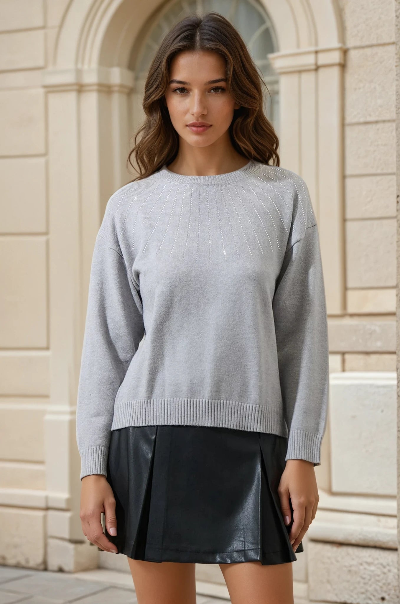 Woman wearing a gray sweater and black skirt standing in front of a stone building.