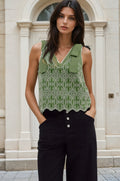 Woman wearing a green lace top and black pants standing in front of a stone building.